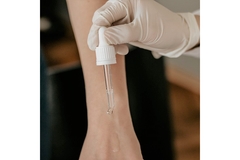 Image A hand with a glove on it and applying a serum onto another hand.